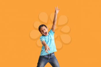 Little African-American boy dancing and singing against color background�