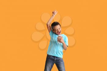 Little African-American boy listening to music and dancing against color background�