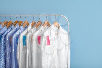 Rack with clothes after dry-cleaning on color background�