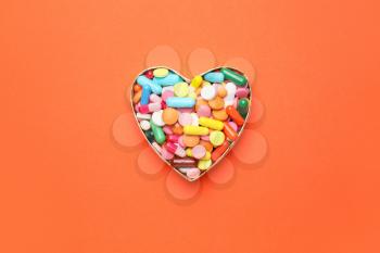 Heart made of pills on color background�