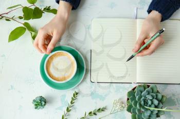 Woman writing in notebook and drinking coffee at table, top view�