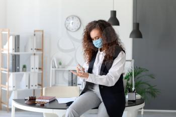 African-American businesswoman with disinfectant in office�