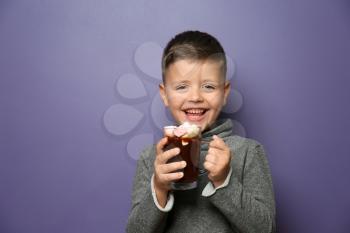 Cute little boy with glass cup of hot chocolate on color background�