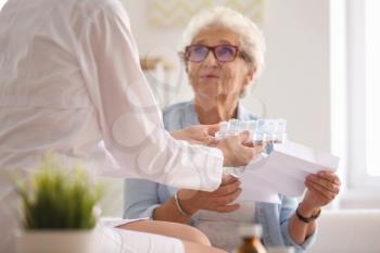 Doctor giving medicine and instruction to senior woman at home 