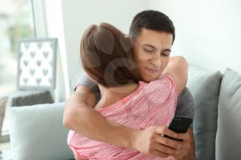 Young cheater texting lover while hugging his girlfriend at home�