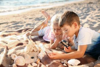 Cute little children looking at sea shells through magnifying glass on beach�