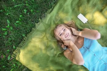 Beautiful young woman listening to music while lying on green grass outdoors�