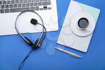Laptop with headset, notebook and coffee on color background�