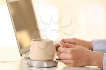 Woman taking cup of coffee from heater on table�