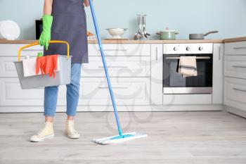 Young woman mopping floor in kitchen�