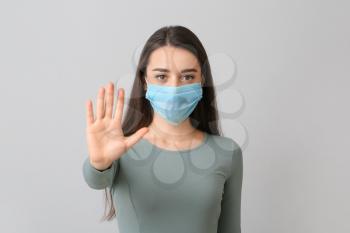 Young woman in medical mask showing STOP gesture against grey background�