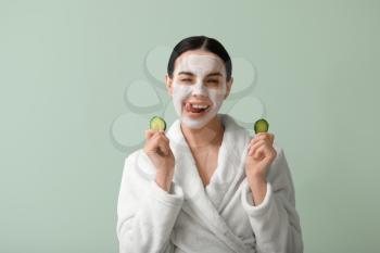 Beautiful young woman with cucumber slices and facial mask on color background�
