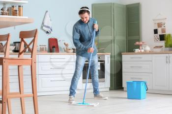 Handsome young man mopping floor in kitchen�