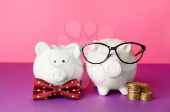 Piggy banks with bowtie and glasses on color background�