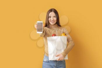 Young woman with food in bag and mobile phone on color background�