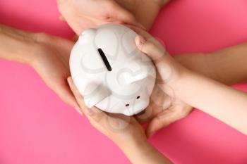 Hands of family with piggy bank on color background�