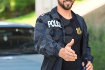 Handsome male police officer giving hand for handshake outdoors�