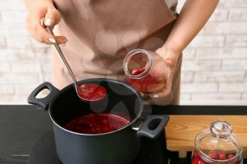 Woman making sweet strawberry jam in kitchen�