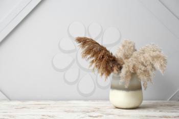 Beautiful vase with pampas grass on wooden table against gray background�