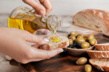 Woman pouring tasty olive oil onto bread slice, closeup�