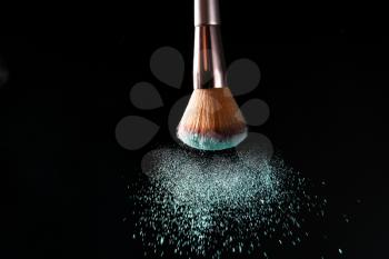 Makeup brush and burst of cosmetics on dark background�