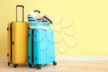 Packed suitcases with beach bag and hat near color wall�