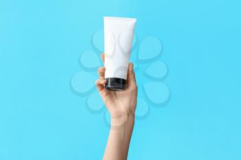 Hand with cosmetic bottle on color background�