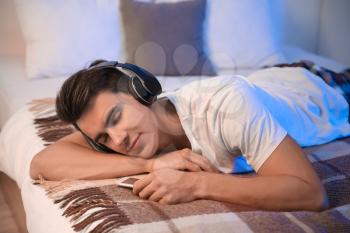Young man listening to music in bedroom at home�