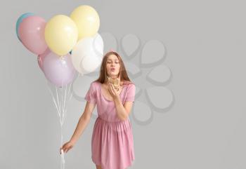 Young woman with balloons and birthday cake on grey background�
