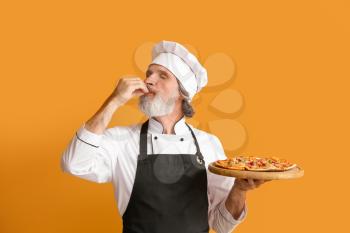Mature male chef with tasty pizza on color background�