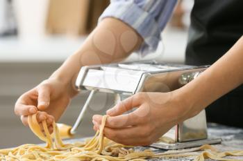 Woman making pasta with machine at table in kitchen�
