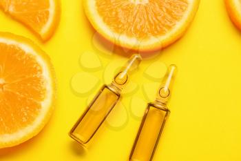 Ampules with vitamin C injection and orange fruit slices on color background�