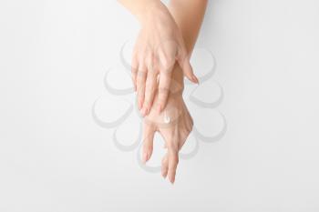 Young woman applying cream on hands against light background�