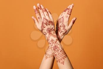 Beautiful female hands with henna tattoo on color background�