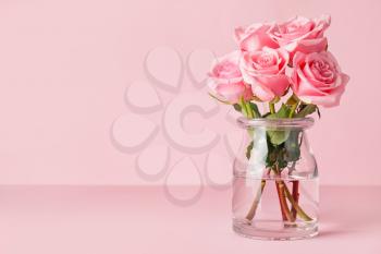 Beautiful pink roses in vase on color background�