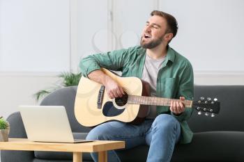 Young man taking music lessons online at home�