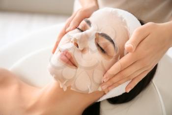 Cosmetologist applying sheet mask on woman's face in beauty salon�