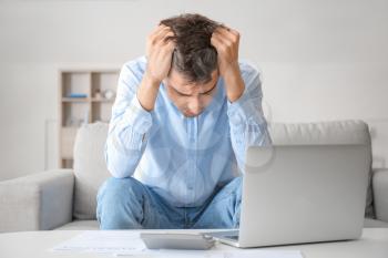 Stressed man with laptop and calculator at home. Bankruptcy concept�