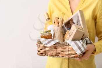 Woman holding gift basket with products on light background, closeup�