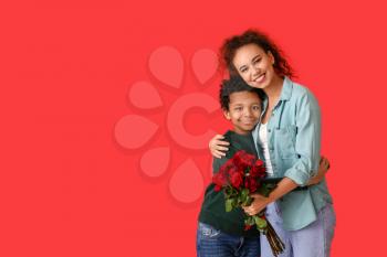 African-American boy and his mother with flowers on color background�