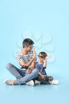 Father and little son playing video games on color background�