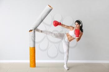 Sporty female boxer kicking cigarette near light wall�