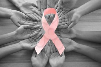 Female hands with pink ribbon on wooden background, top view. Breast cancer concept�