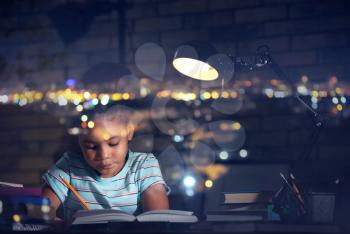 Double exposure of little African-American girl doing homework and illuminated city in evening�