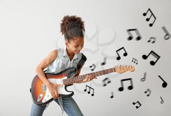 African-American girl playing guitar against light background�