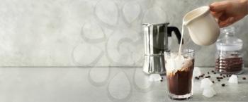Woman pouring milk into glass with cold coffee on grey background with space for text�