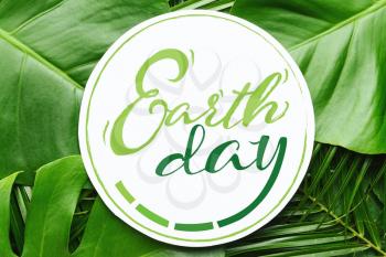 Card with text EARTH DAY on green tropical leaves�