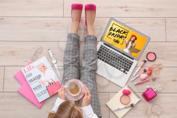 Young woman drinking coffee while using laptop for shopping at home. Black Friday sale�