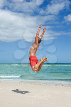 muscular young man jumping on the beach 