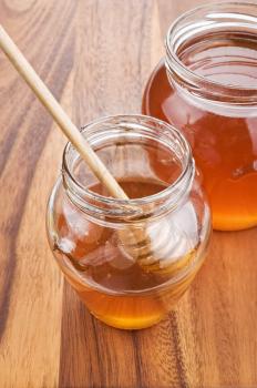 glass jar with honey and wooden stick on wood background 